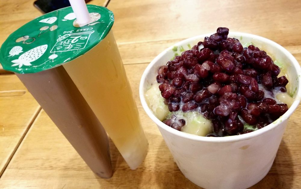 Boba milk tea next to a cup of shaved ice with red bean