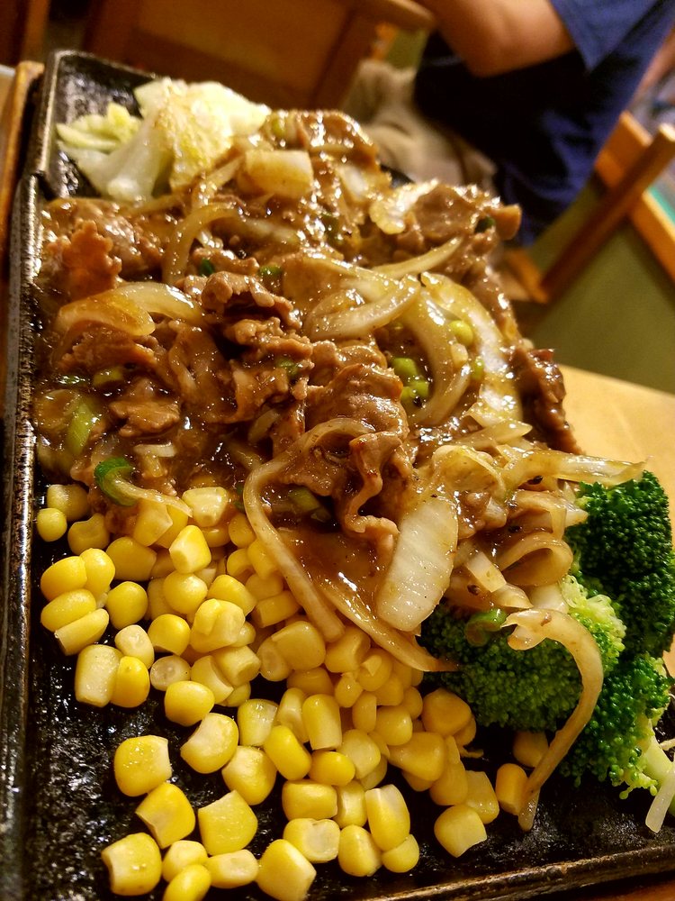 Sizzling beef with onions, corn and broccoli on a hot plate