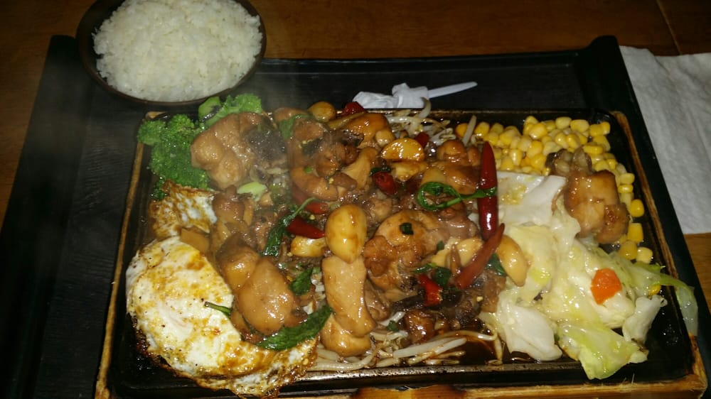 Sizzling plate of chicken with vegetables, corn and a fried egg, served with rice